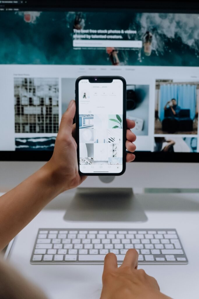 pexels photo 5082576 5082576 Person uses a smartphone in front of a computer screen displaying stock photos, showcasing modern technology use.